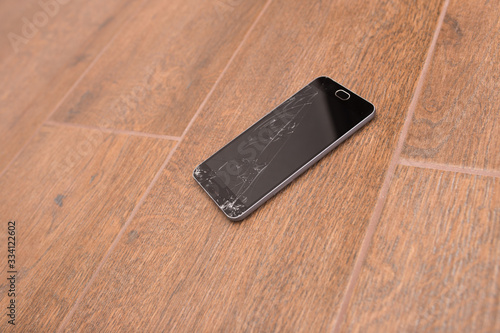 A broken phone is on the floor. Smartphone cracked screen closeup.