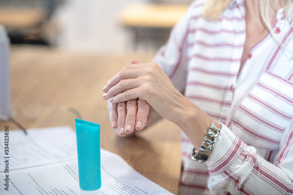 Female hands rubbing hand cream above desk