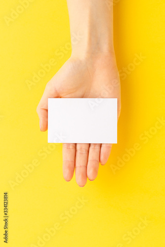 Woman’s hand holding business card on yellow background. Mockup. Close up