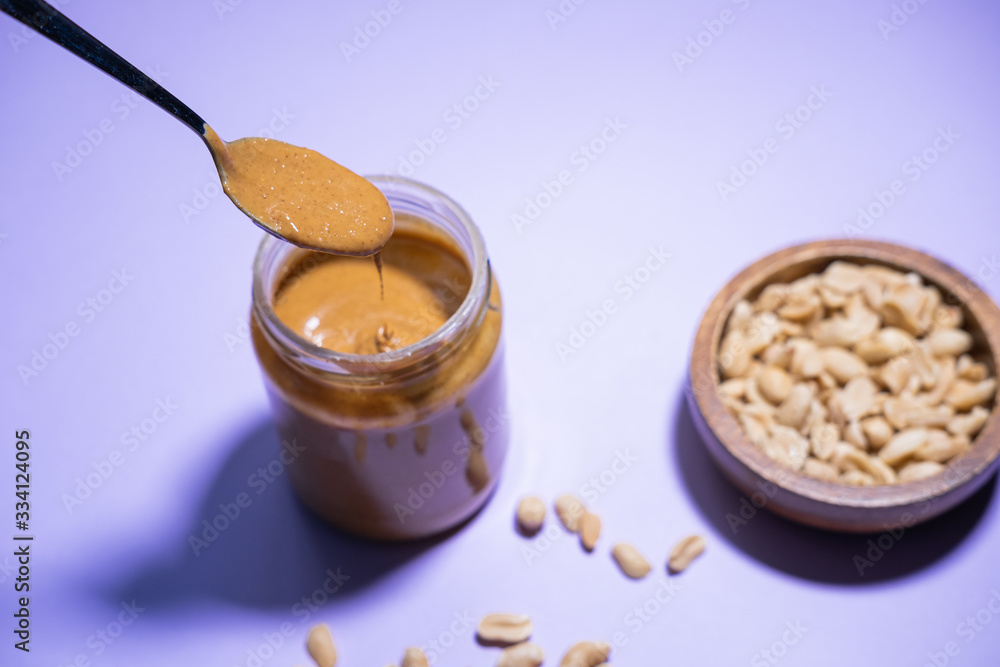 Spoon full of peanut butter, falling into a glass jar on purple background. Vegan product. Spoon full of peanut butter, falling into a glass jar on purple background. Vegan product.