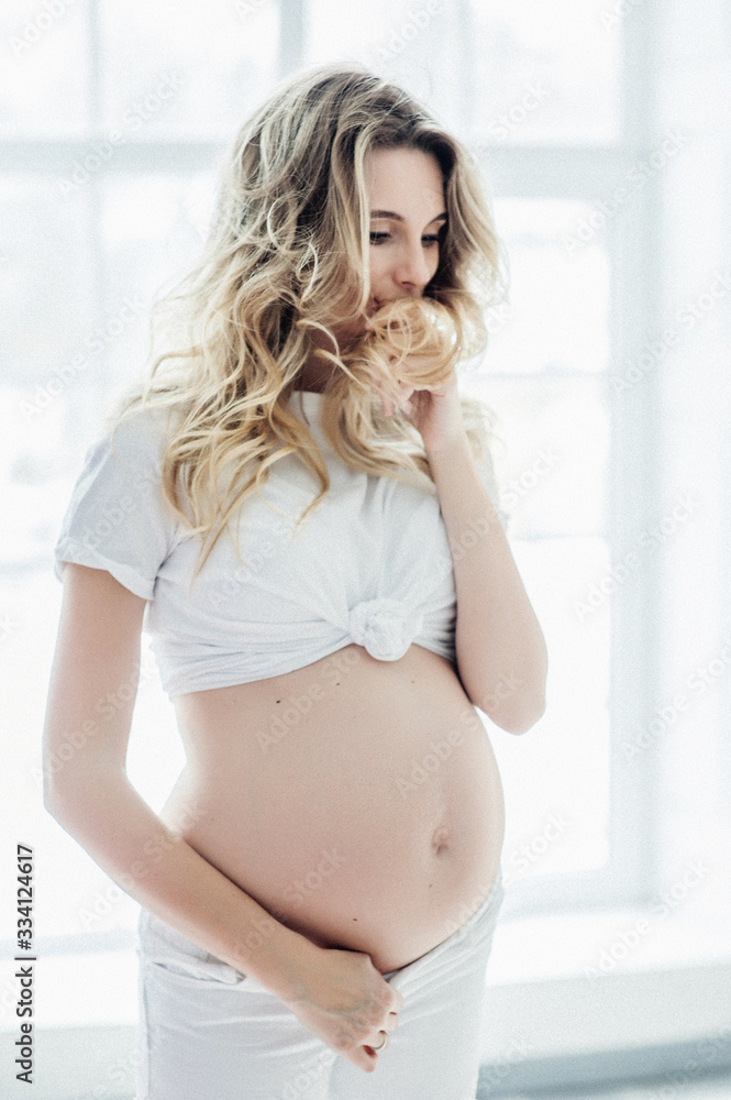 A pregnant European girl stands by the window. Studio photo shoot. Soft focus. A pregnant European girl stands by the window. Studio photo shoot. Soft focus.