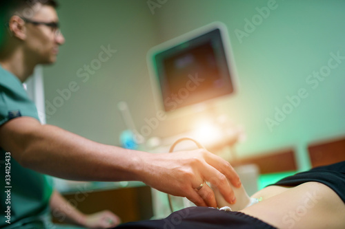 A young male doctor makes a patient an ultrasound of the abdominal cavity. Ultrasound scanner in the hands of a doctor.