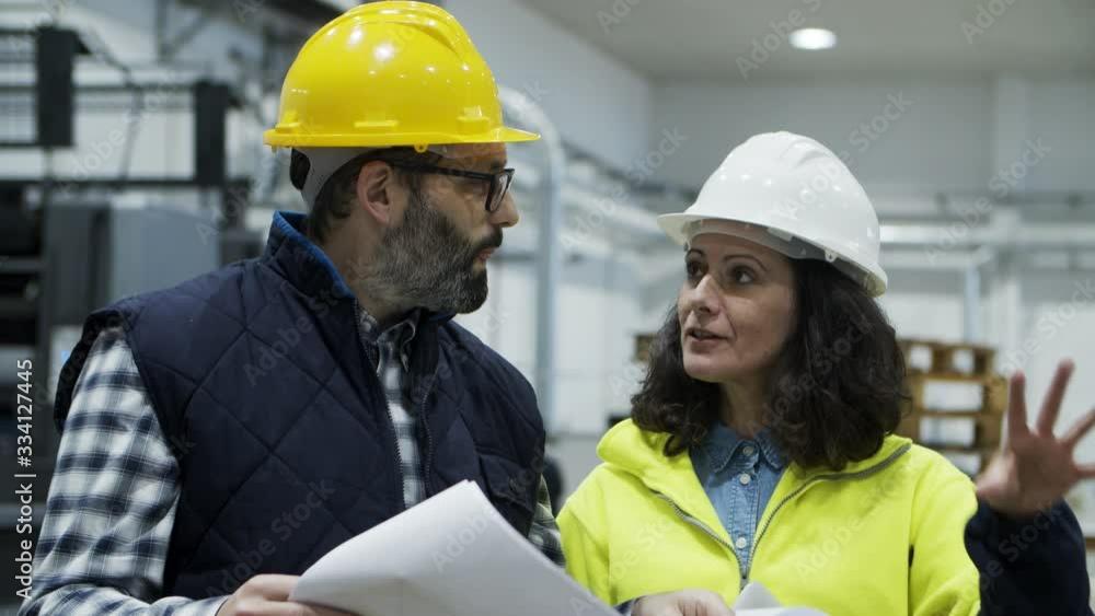 Focused workers talking while inspecting quality of print. Concentrated printing technicians looking at blueprint at factory. Print manufacturing concept Focused workers talking while inspecting quality of print. Concentrated printing technicians looking at blueprint at factory. Print manufacturing concept