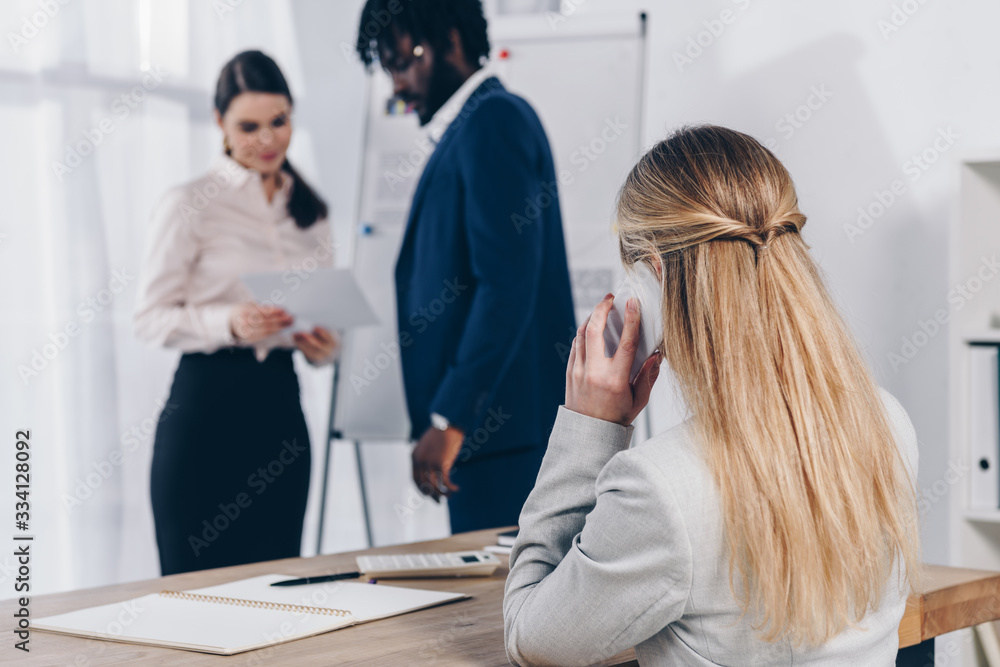 Fototapeta premium Multicultural recruiters with paper near flip chart and employee talking on smartphone in office