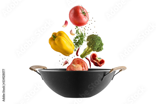 Fresh multicolored vegetables fly over a wok frying pan. White isolated background.