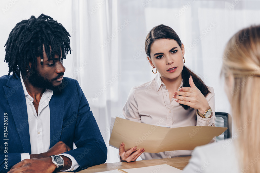 Selective focus of multiethnic recruiters conducting job interview with employee at table in office Selective focus of multiethnic recruiters conducting job interview with employee at table in office