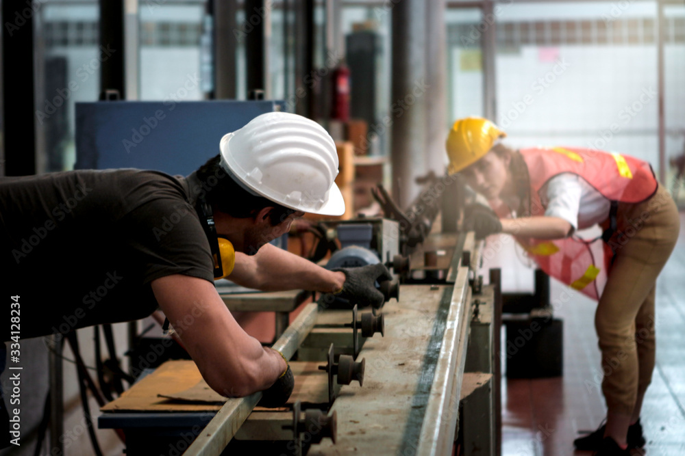 Industrial engineer worker woman and man wearing helmet working together with mechanism at manufacturing plant factory, young people working in industry Industrial engineer worker woman and man wearing helmet working together with mechanism at manufacturing plant factory, young people working in industry