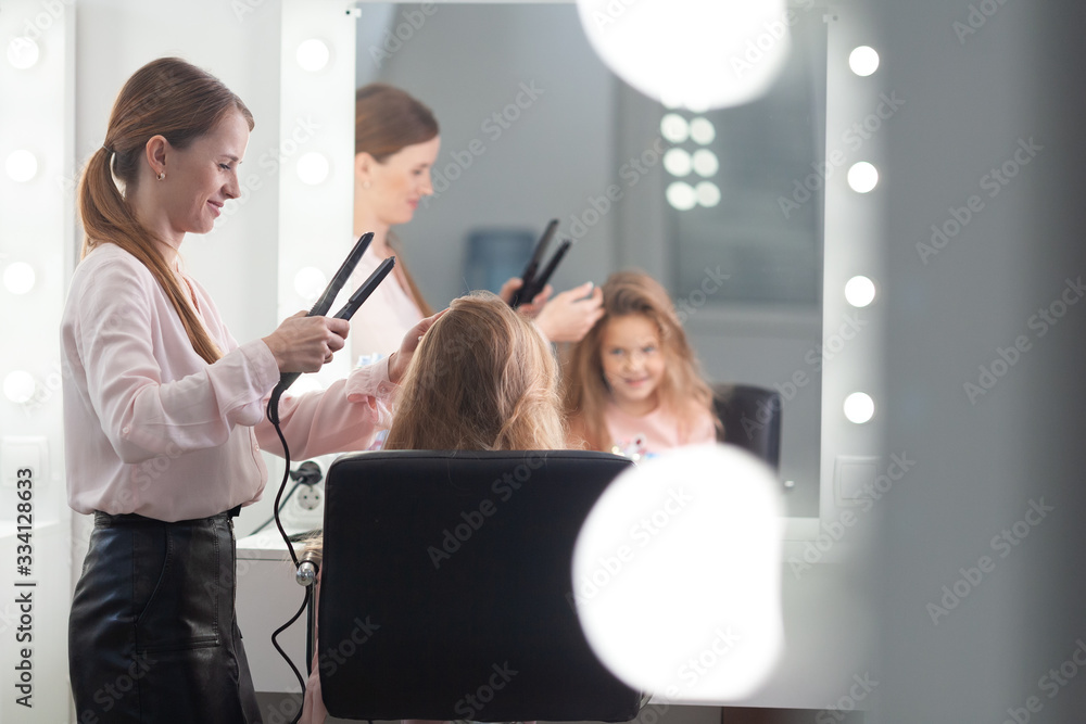 The work of the stylist on hairstyles in a bright salon, the girl makes curls and braids braids of a small beautiful model, The work of the stylist on hairstyles in a bright salon, the girl makes curls and braids braids of a small beautiful model,