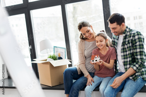 mortgage, family and real estate concept - happy mother, father and little daughter with house model and stuff in boxes moving to new home