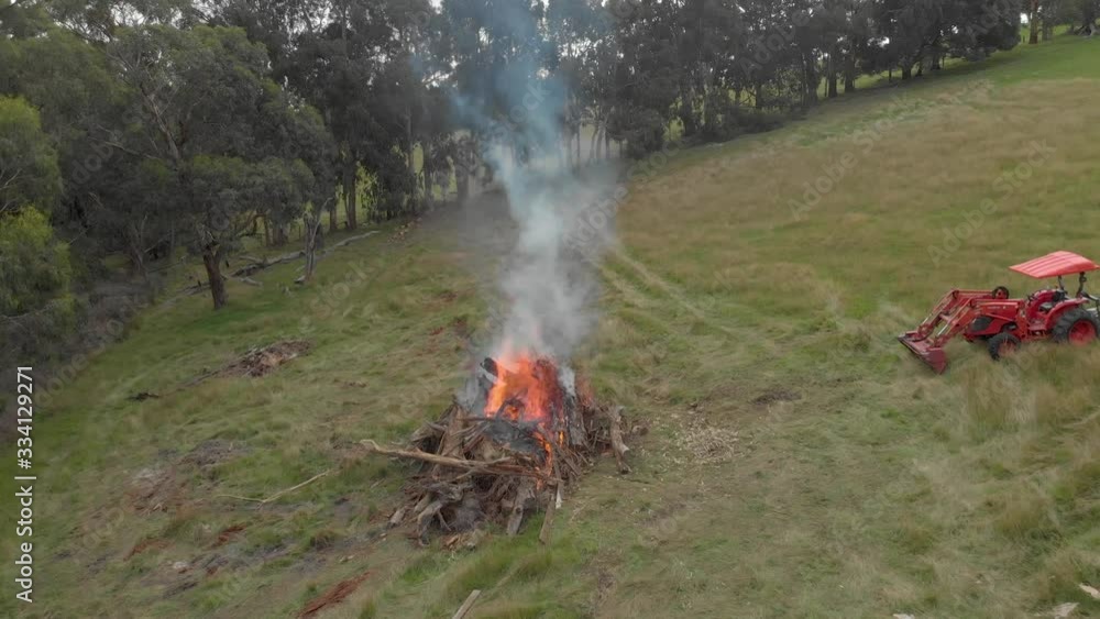 forward moving aerial over a big bonfire on a rural bush property flying over the smoke with a tractor parked nearby. forward moving aerial over a big bonfire on a rural bush property flying over the smoke with a tractor parked nearby.
