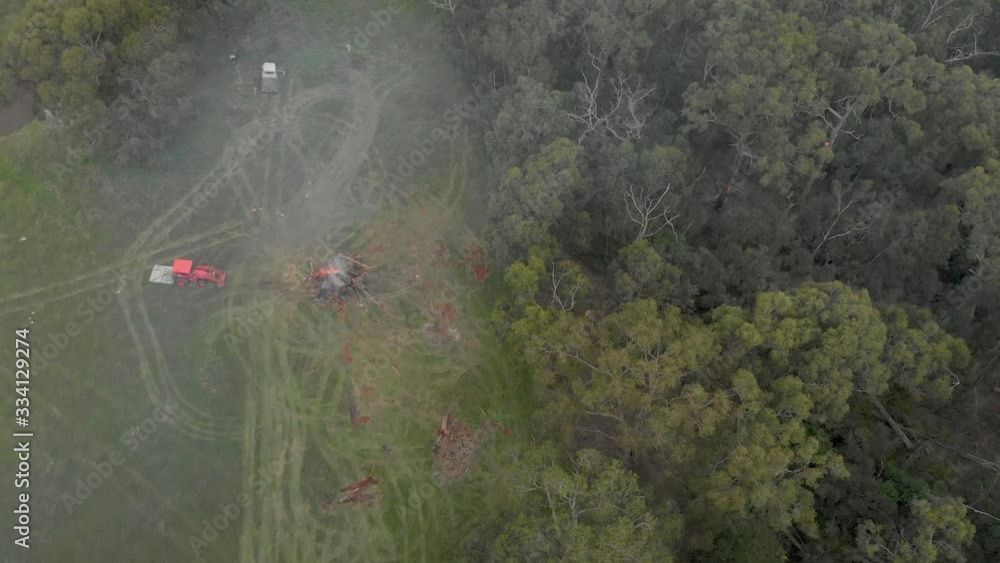 Aerial shot orbiting around a bonfire on a farm with a parked tractor on a rural bush property. Aerial shot orbiting around a bonfire on a farm with a parked tractor on a rural bush property.