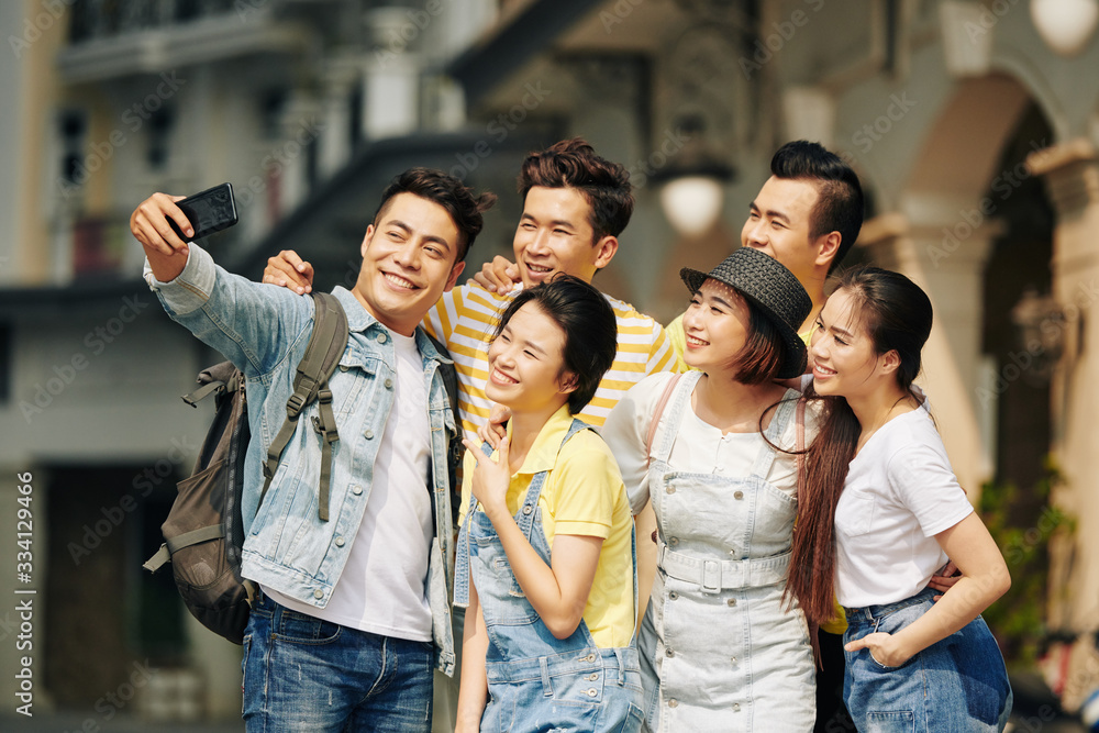 Happy Vietnamese young man taking selfie with group of friends when standing in the street Happy Vietnamese young man taking selfie with group of friends when standing in the street