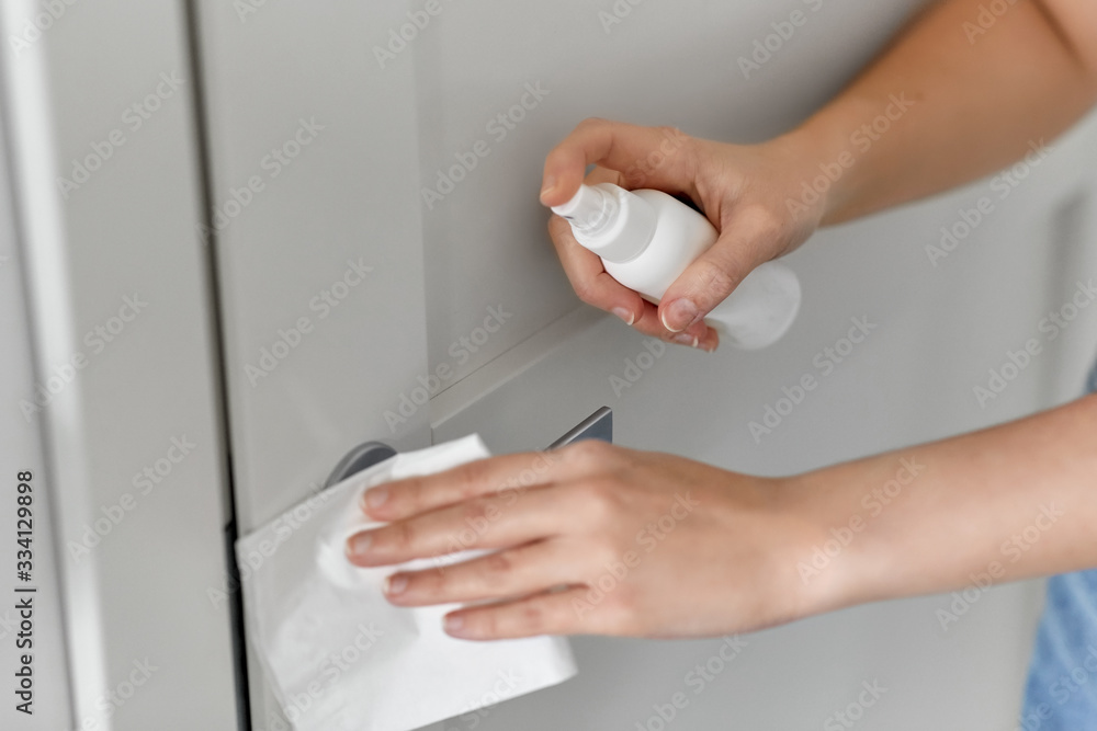 hygiene, health care and safety concept - close up of hands cleaning door handle surface with disinfectant spray and tissue hygiene, health care and safety concept - close up of hands cleaning door handle surface with disinfectant spray and tissue