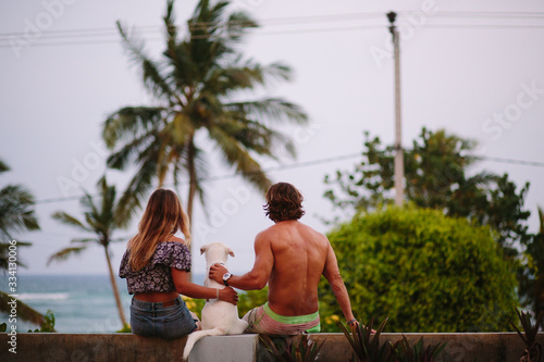 
Young couple girl and guy sit on the roof with a white dog and look at the ocean and palm trees