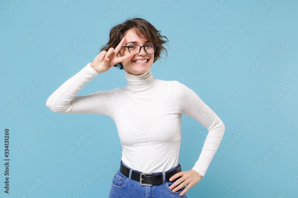 Smiling young brunette woman girl in casual white clothes, eyeglasses posing isolated on pastel blue background studio portrait. People lifestyle concept. Mock up copy space. Showing victory sign. Smiling young brunette woman girl in casual white clothes, eyeglasses posing isolated on pastel blue background studio portrait. People lifestyle concept. Mock up copy space. Showing victory sign.