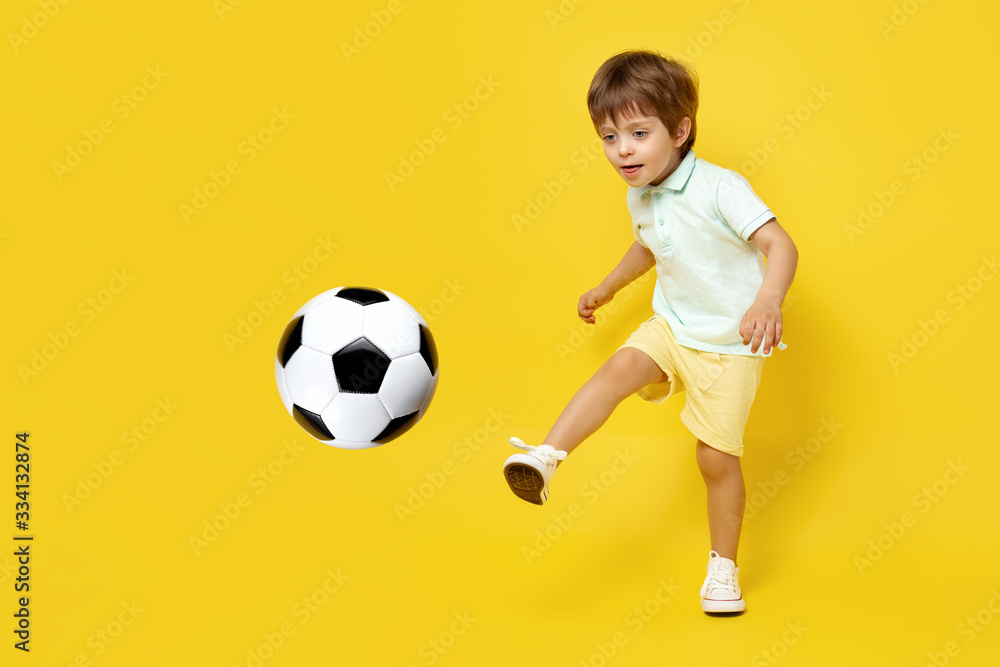 Charming little kid in casual summer outfit play with soccer ball over yellow background. Charming little kid in casual summer outfit play with soccer ball over yellow background.