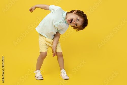 Adorable funny kid listening music and dance over yellow background.