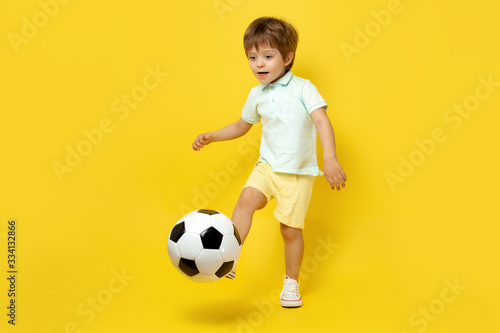 Cute little kid in casual summer outfit play with soccer ball over yellow background. © Screaghin