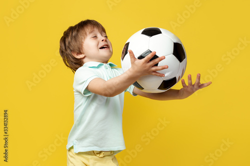 Funny little kid in casual summer outfit try to catch the ball soccer ball over yellow background.
