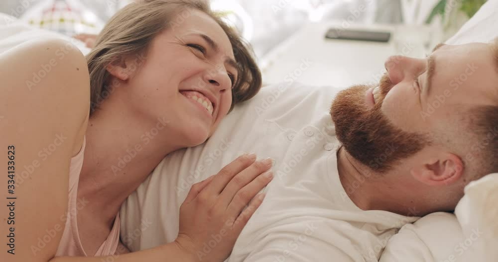 Close up view of happy couple lying on bed in early morning, talking andlaughing. Beautiful woman and her handsome husband having good time.Concept of family and relationship. Close up view of happy couple lying on bed in early morning, talking andlaughing. Beautiful woman and her handsome husband having good time.Concept of family and relationship.