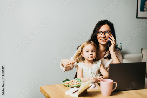 Woman works at home on a laptop with a child. Mom works remotely at home. Lifestyle photos.