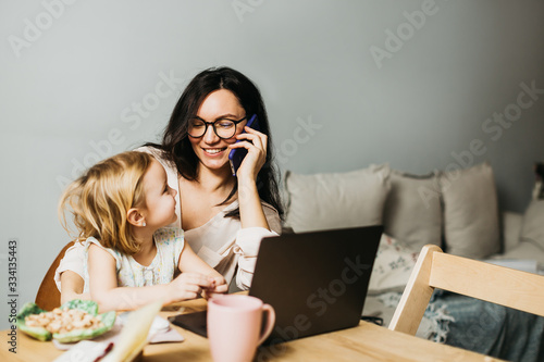Woman works at home on a laptop with a child. Mom works remotely at home. Lifestyle photos.
