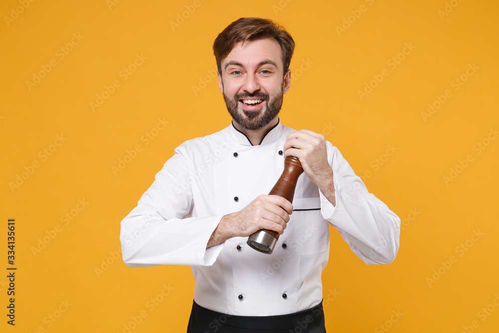 Funny young bearded male chef cook or baker man in white uniform shirt posing isolated on yellow orange wall background studio portrait. Cooking food concept. Mock up copy space. Hold pepper shaker. Funny young bearded male chef cook or baker man in white uniform shirt posing isolated on yellow orange wall background studio portrait. Cooking food concept. Mock up copy space. Hold pepper shaker.