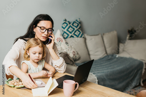 Woman works at home on a laptop with a child. Mom works remotely at home. Lifestyle photos.