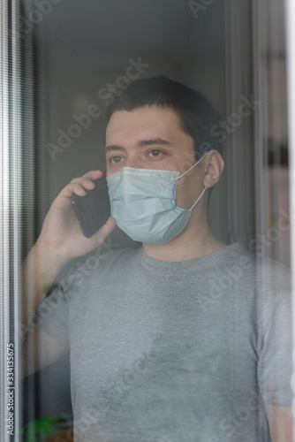 A young man in a medical mask remains isolated at home for self-quarantine. The concept of home quarantine, prevention of COVID-19, the situation with the coronavirus outbreak. A person working from 