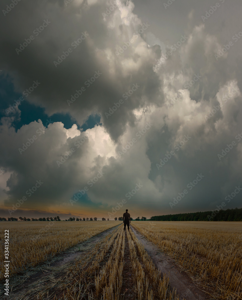 Man standing on empty field under dark cloudy sky
