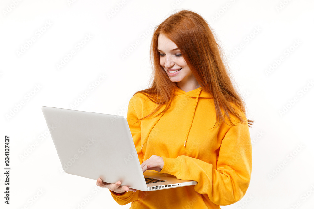 Naklejka premium Smiling young redhead woman girl in yellow hoodie posing isolated on white background studio portrait. People sincere emotions lifestyle concept. Mock up copy space. Working on laptop pc computer.