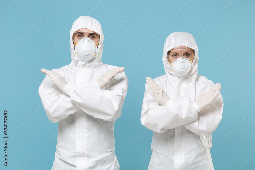 Two people in protective suits respirator masks isolated on blue background studio. Epidemic pandemic new rapidly spreading coronavirus 2019-ncov originating in Wuhan China, virus concept stop gesture Two people in protective suits respirator masks isolated on blue background studio. Epidemic pandemic new rapidly spreading coronavirus 2019-ncov originating in Wuhan China, virus concept stop gesture