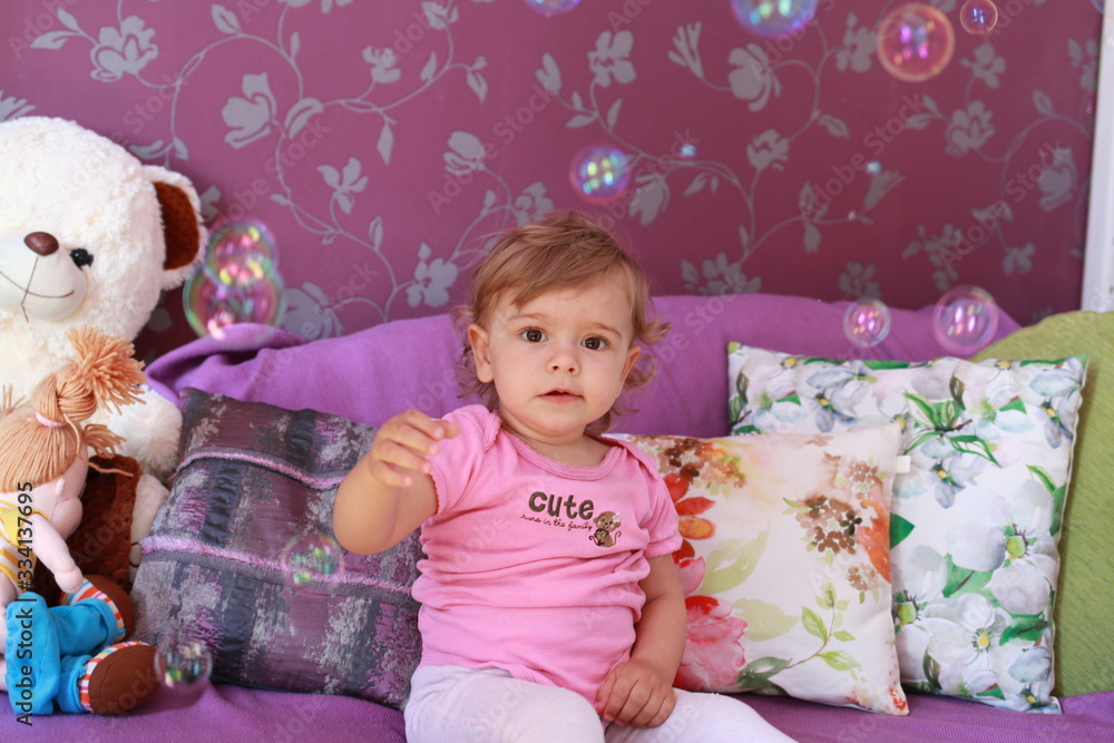 Cute little Caucasian girl one year old plays in her room with soap bubbles, laughs merrily, close-up. Childhood, leisure, games. Cute little Caucasian girl one year old plays in her room with soap bubbles, laughs merrily, close-up. Childhood, leisure, games.