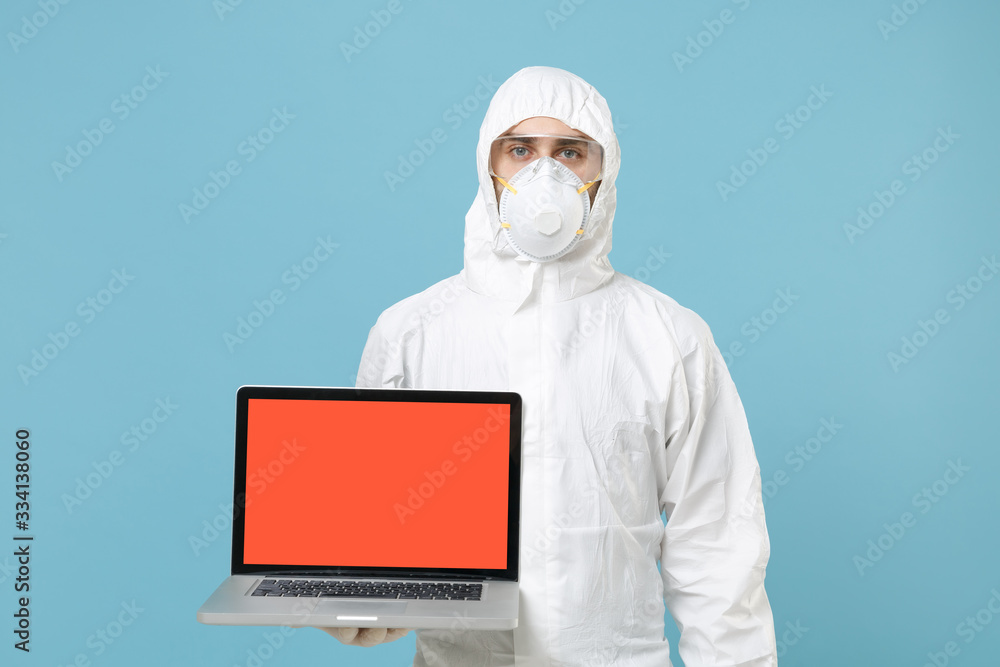 Man in white protective suit respirator mask hold laptop pc blank empty screen isolated on blue background studio Epidemic pandemic rapidly spreading coronavirus 2019-ncov medicine flu virus concept. Man in white protective suit respirator mask hold laptop pc blank empty screen isolated on blue background studio Epidemic pandemic rapidly spreading coronavirus 2019-ncov medicine flu virus concept.