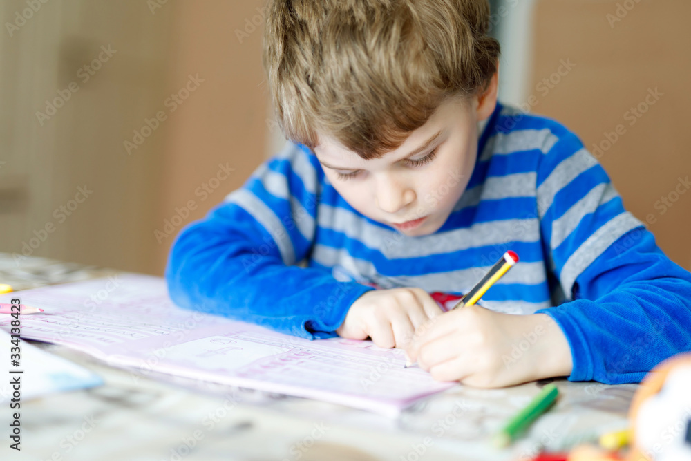 Hard-working happy school kid boy making homework during quarantine time from corona pandemic disease. Healthy child writing with pen, staying at home. Homeschooling concept Hard-working happy school kid boy making homework during quarantine time from corona pandemic disease. Healthy child writing with pen, staying at home. Homeschooling concept