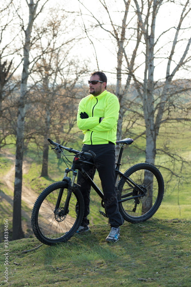 Cyclist in pants and green jacket on a modern carbon hardtail bike with an air suspension fork. The guy on the top of the hill rides a bike.