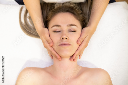 Young blond woman receiving a head massage in a spa center.
