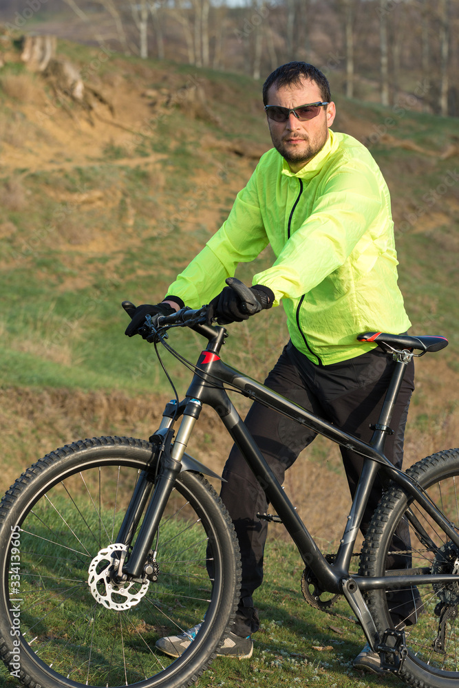Cyclist in pants and green jacket on a modern carbon hardtail bike with an air suspension fork. The guy on the top of the hill rides a bike. Cyclist in pants and green jacket on a modern carbon hardtail bike with an air suspension fork. The guy on the top of the hill rides a bike.