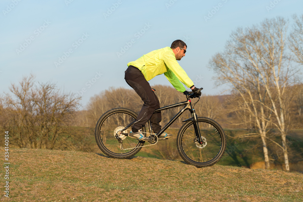 Cyclist in pants and green jacket on a modern carbon hardtail bike with an air suspension fork. The guy on the top of the hill rides a bike.