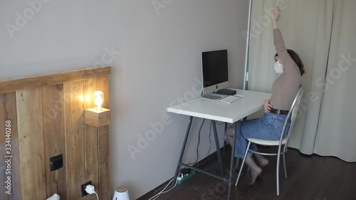 Young girl in a protective mask does a warm-up sitting at a table with a computer in quarantine at home.Coronavirus.COVID-19 photo