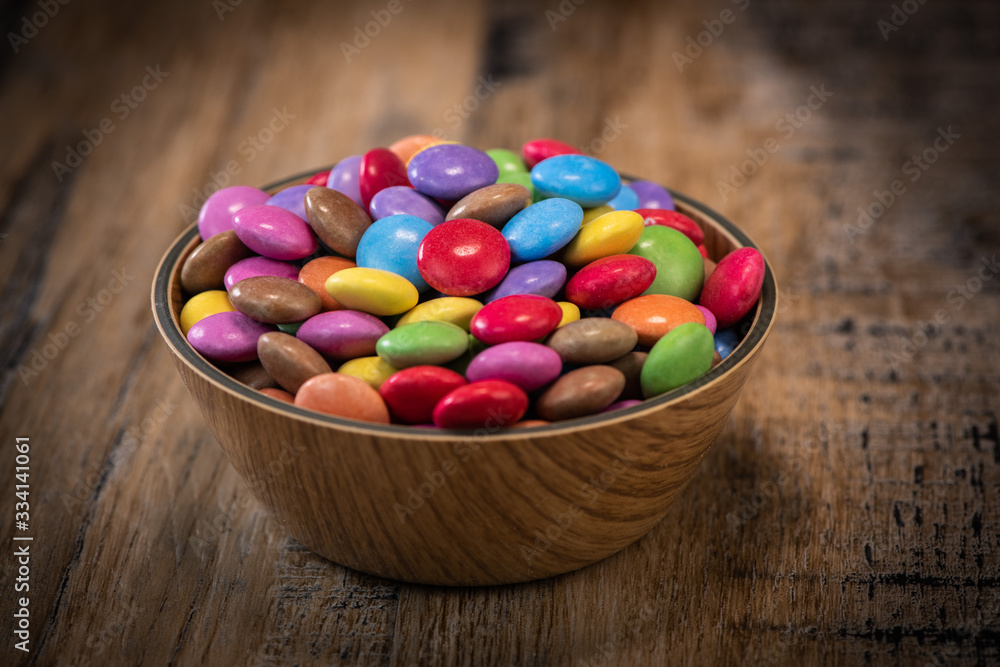 Colorful candies in a wooden bowl case isolated on wood background Colorful candies in a wooden bowl case isolated on wood background