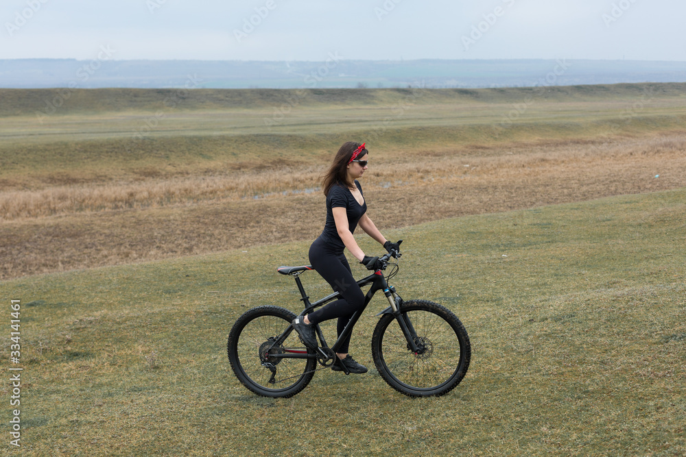 Girl on a mountain bike on offroad, beautiful portrait of a cyclist in rainy weather, Fitness girl rides a modern carbon fiber mountain bike in sportswear. Close-up portrait of a girl in red bandana.