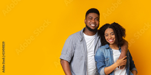 Portrait of smiling black couple hugging and posing over yellow background