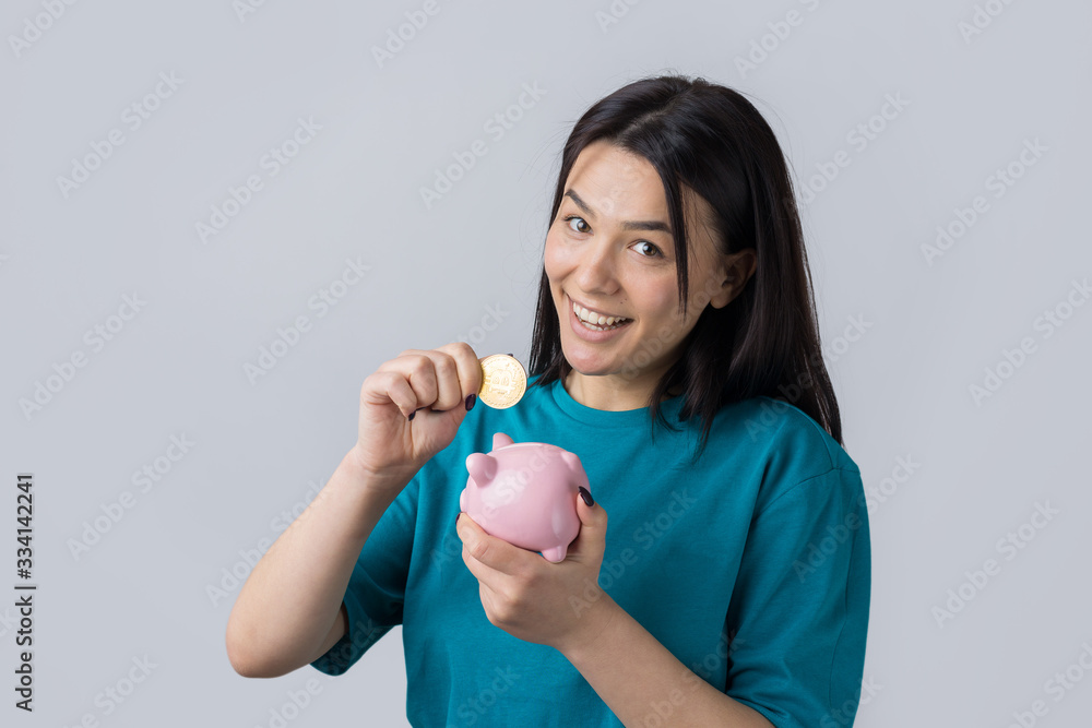 The girl holds a pink piggy bank and a coin in her hands. The concept of wealth and accumulation. The girl holds a pink piggy bank and a coin in her hands. The concept of wealth and accumulation.