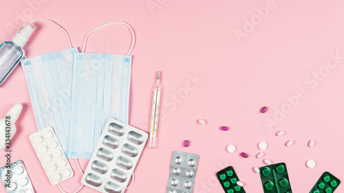Protective medicine mask, antiseptic thermometer and pills on pink background, flat lay. Concept of doctor table and health care.