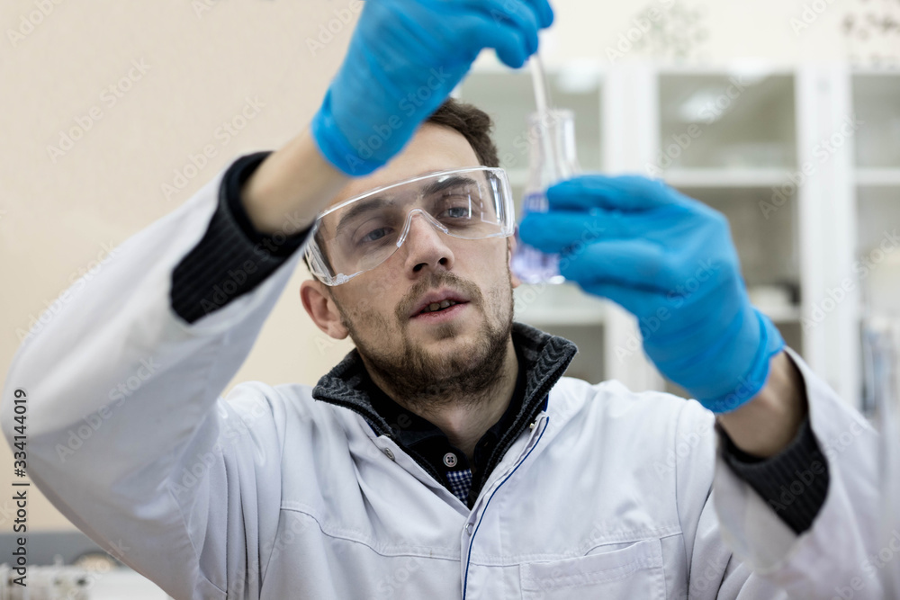 A scientist studies a chemical substance in a flask in a research laboratory. Chemist. Virologist. Microbiologist. A scientist studies a chemical substance in a flask in a research laboratory. Chemist. Virologist. Microbiologist.