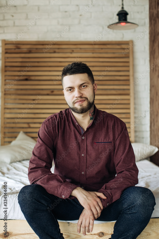 A young bearded man sits in bed and looks into the camera A young bearded man sits in bed and looks into the camera