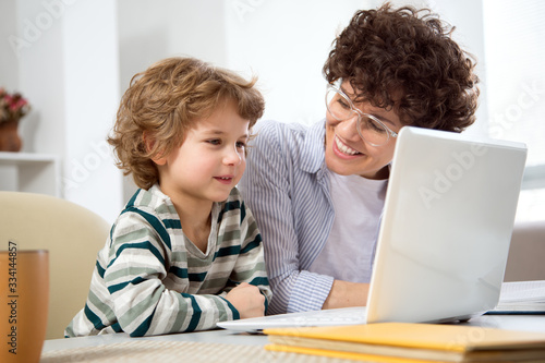 Business woman and her cute little son are using a laptop and smiling while sitting in home office