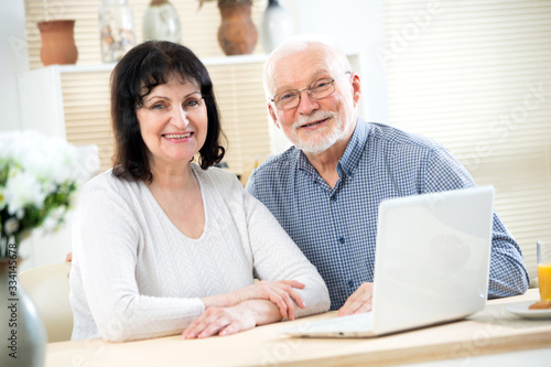 Happy elderly couple with laptop smiling at camera