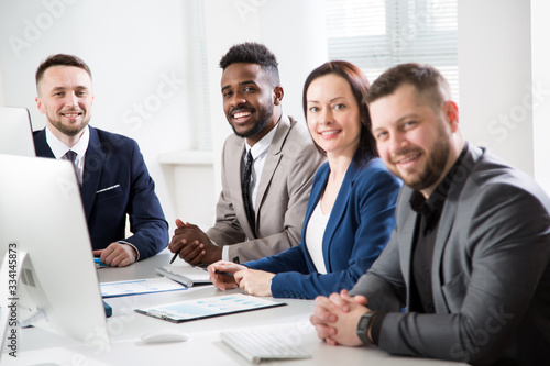 Multy-ethnic group of young business people sitting at the office desk and smiling at camera